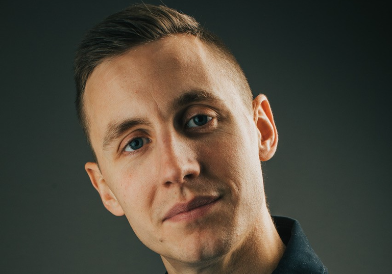 Close-up portrait of Northern Irish comedian and podcast host Shane Todd looking at the camera against a dark grey background.